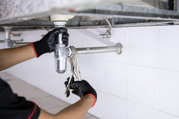 Plumber using a wrench to repair a water pipe under the sink.
