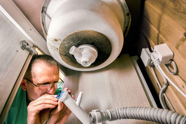 Plumber installs sealing gasket on drain tailpiece with dishwasher hose connection outlet during bottle trap installation under kitchen sink.