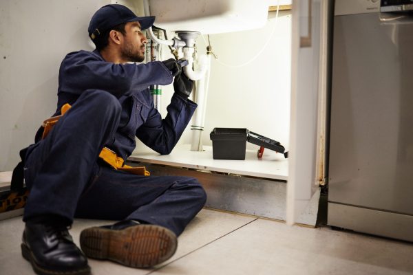 Plumbing, handyman and maintenance with man in kitchen for repair, industrial and inspection. Pipes, tools and safety with male plumber fixing sink for home improvement, drainage and water system.